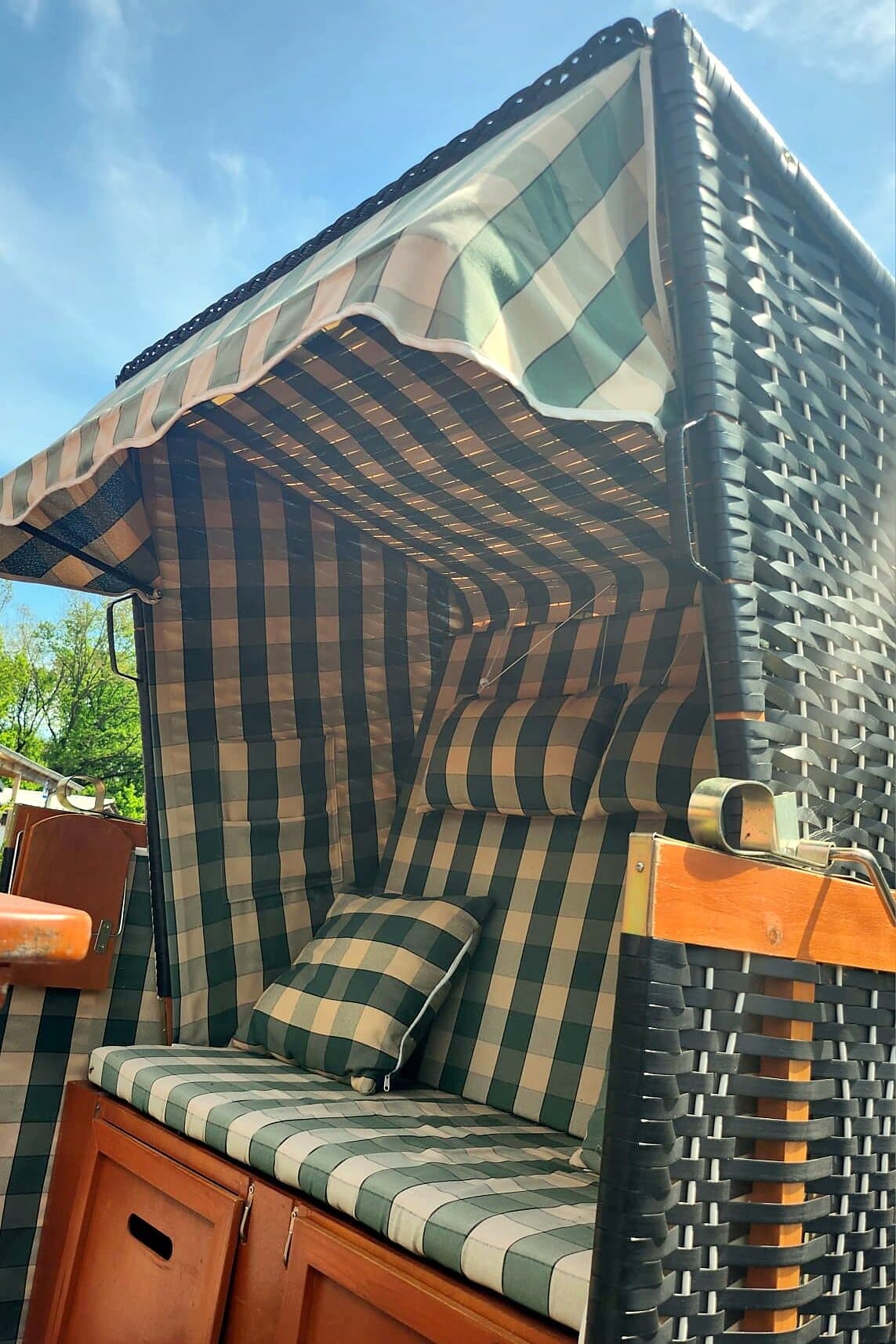 Grün-weiß karierter Strandkorb mit Kissen auf der Terrasse, darüber blauer Himmel